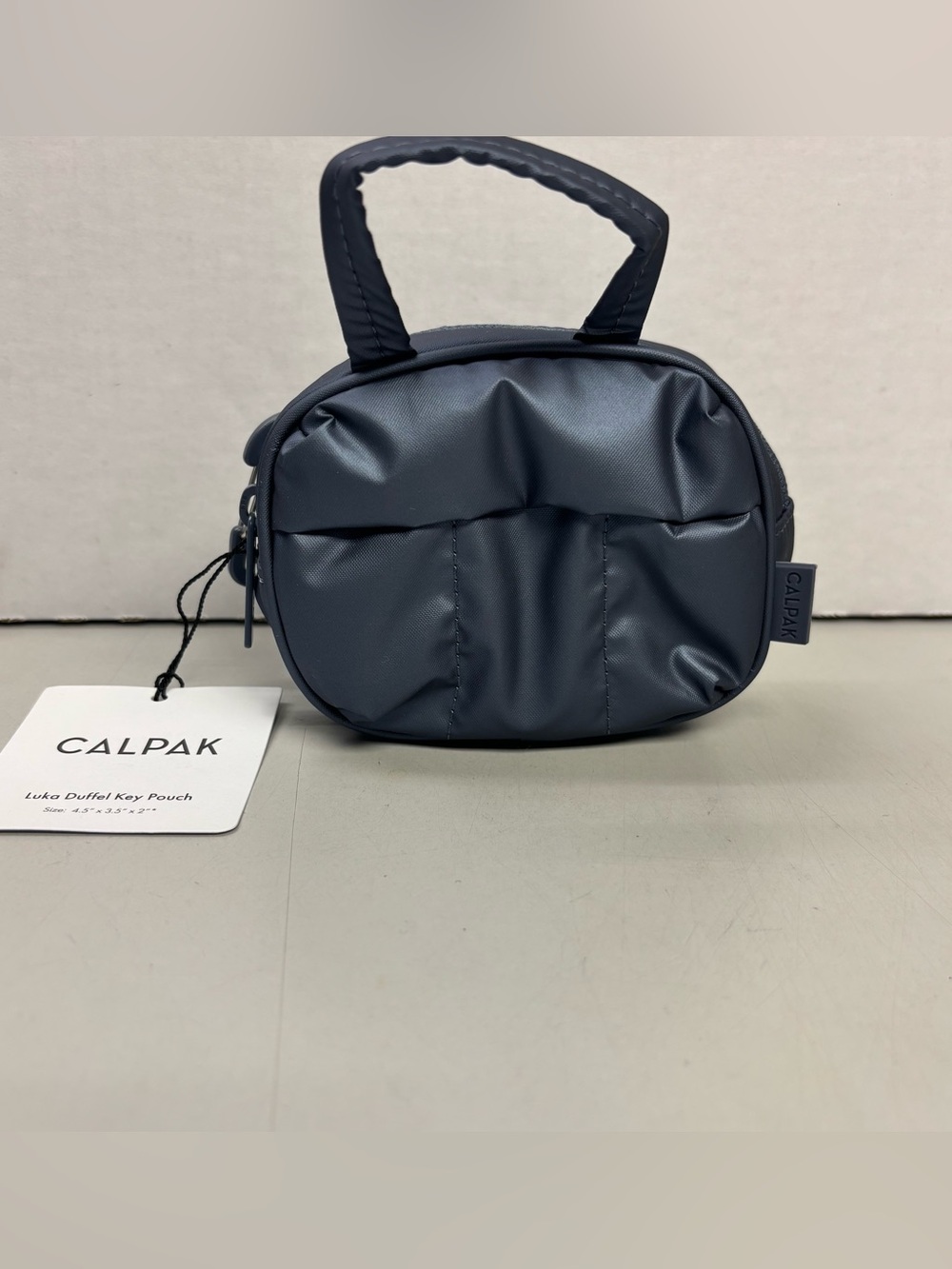 NWT Calpak Luka Duffel Zip Bag Charm in
Metallic Indigo